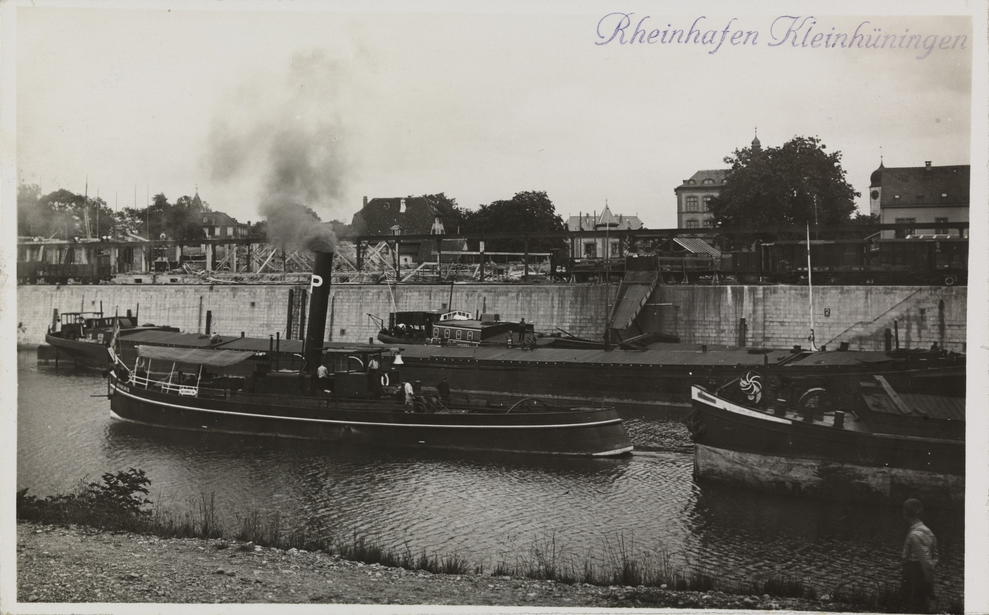 Eine Postkarte von 1924: Ein Dampf-Schraubenschlepper, dessen Namen leider nicht lesbar ist, zieht ein Frachtschiff aus dem Hafenbecken hinaus in die Fahrrinne.