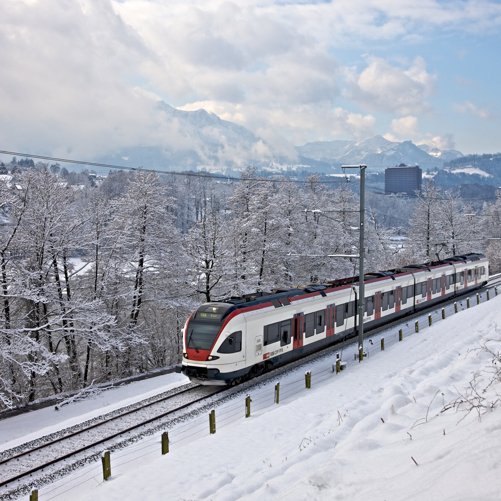 Der Zug RaBe523 der Stadtbahn Zug fährt entlang des Rotsees durch die Winterlandschaft.