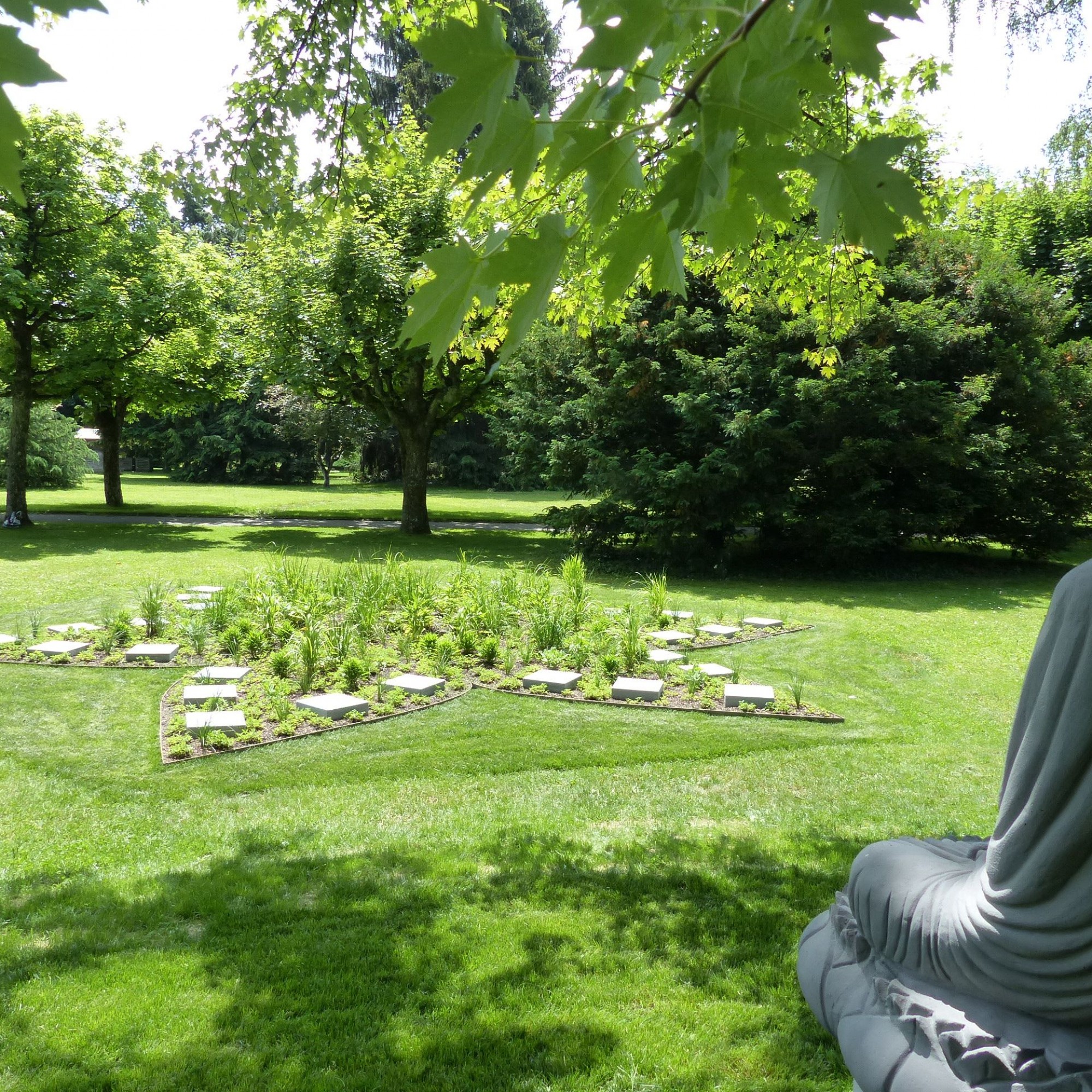 Eine Buddha-Statue sitzt unter einem Silberahorn und wacht über die Lotusblüten.