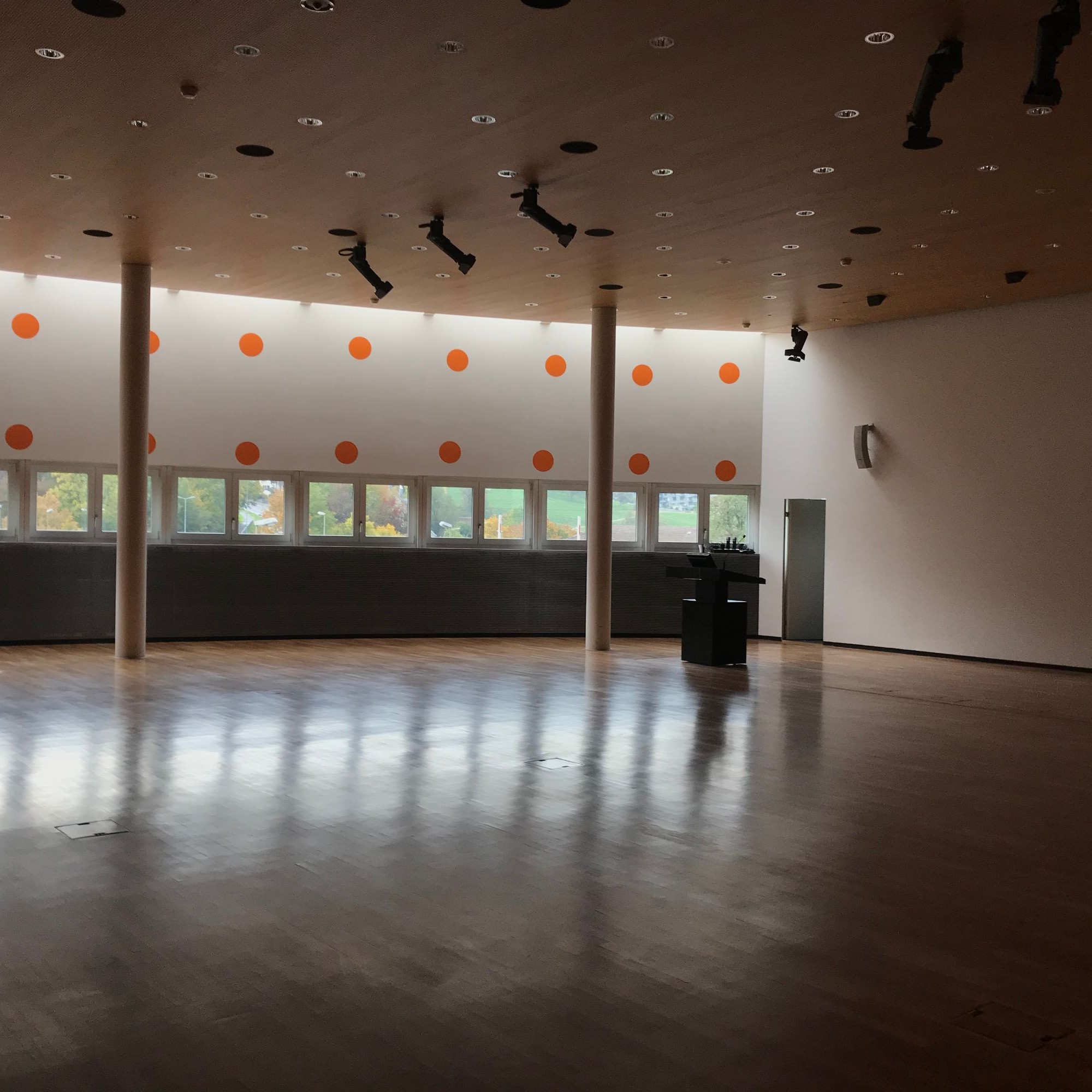 Obwohl die Fenster klein sind, lassen die orangen Punkte und der helle Boden den Konforenzsaal erleuchten.