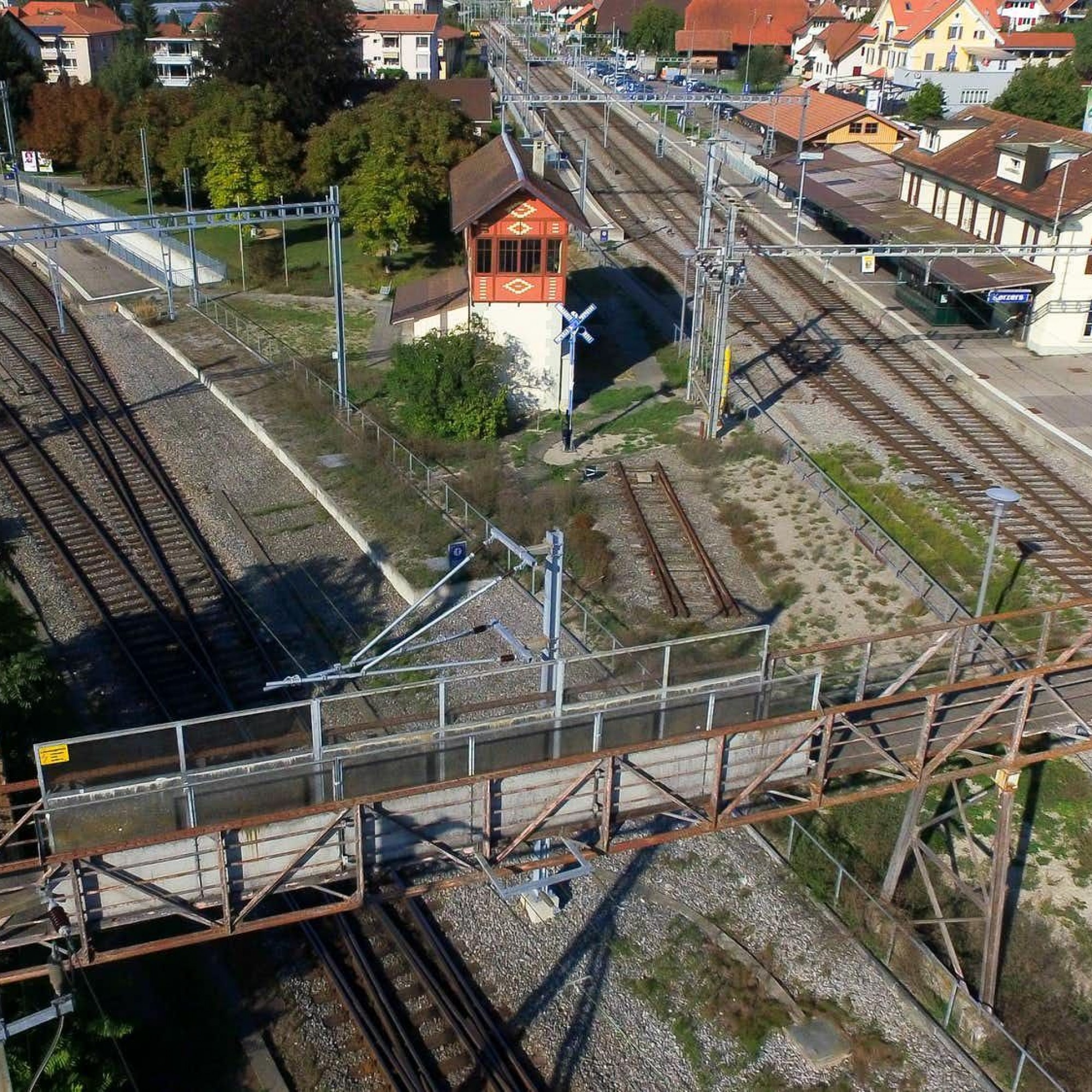 Die Passerelle in Kerzers heute, Richtung Norden gesehen. Auf engstem Raum findet sich ein intaktes Ensemble mit Bahnhofgebäude (rechts), Güterschuppen (rechts hinter Bahnhofgebäude), Stellwerk (Bildmitte) sowie der Passerelle (Vordergrund).