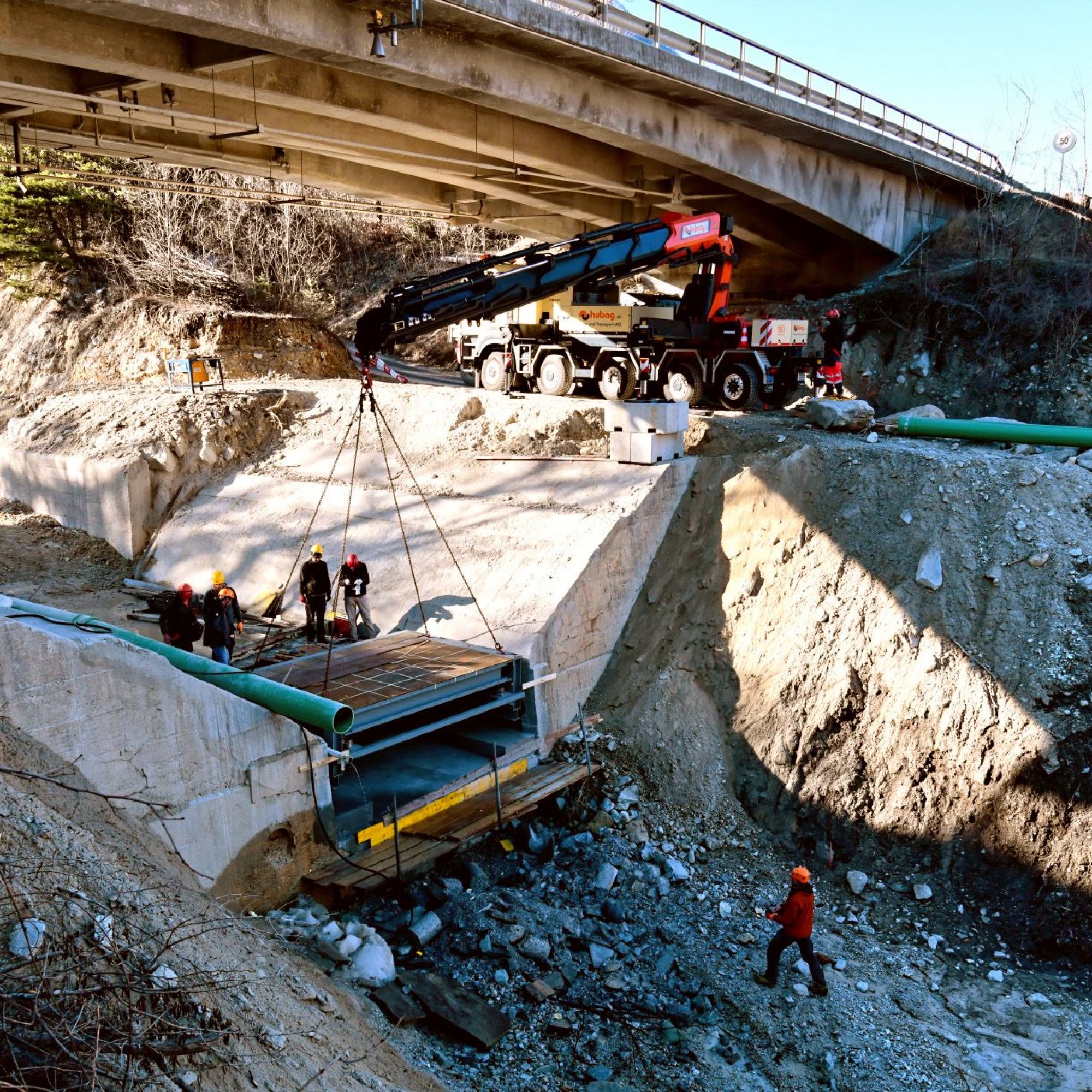 Zentimetergenauer Einbau der über sieben Tonnen schweren Stahlkonstruktion in die Aussparung der aus Beton gefertigten Wildbachsperre unter der Kantonsstrassenbrücke über den Illgraben.