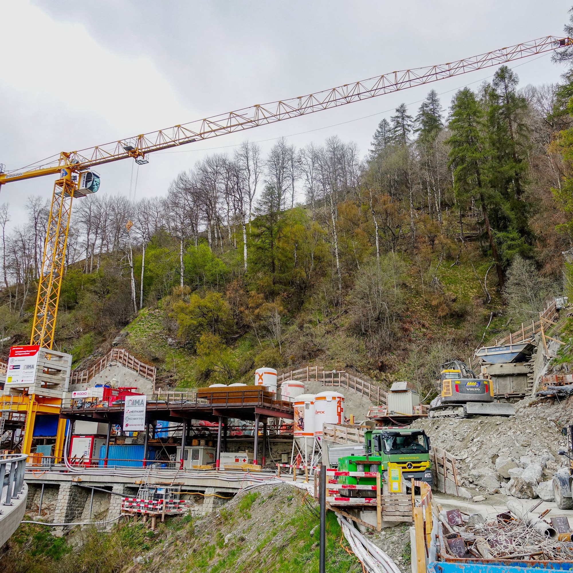 Auf engstem Raum zwischen den Tunnelportalen befinden sich die Zufahrt zum Magnacuntunnel (rechts) und die Baustelleneinrichtung, die teilweise auf der alten Strasse zu stehen kam. Belieferung und Abtransport erfolgen über die neue Kantonsstrasse (links v