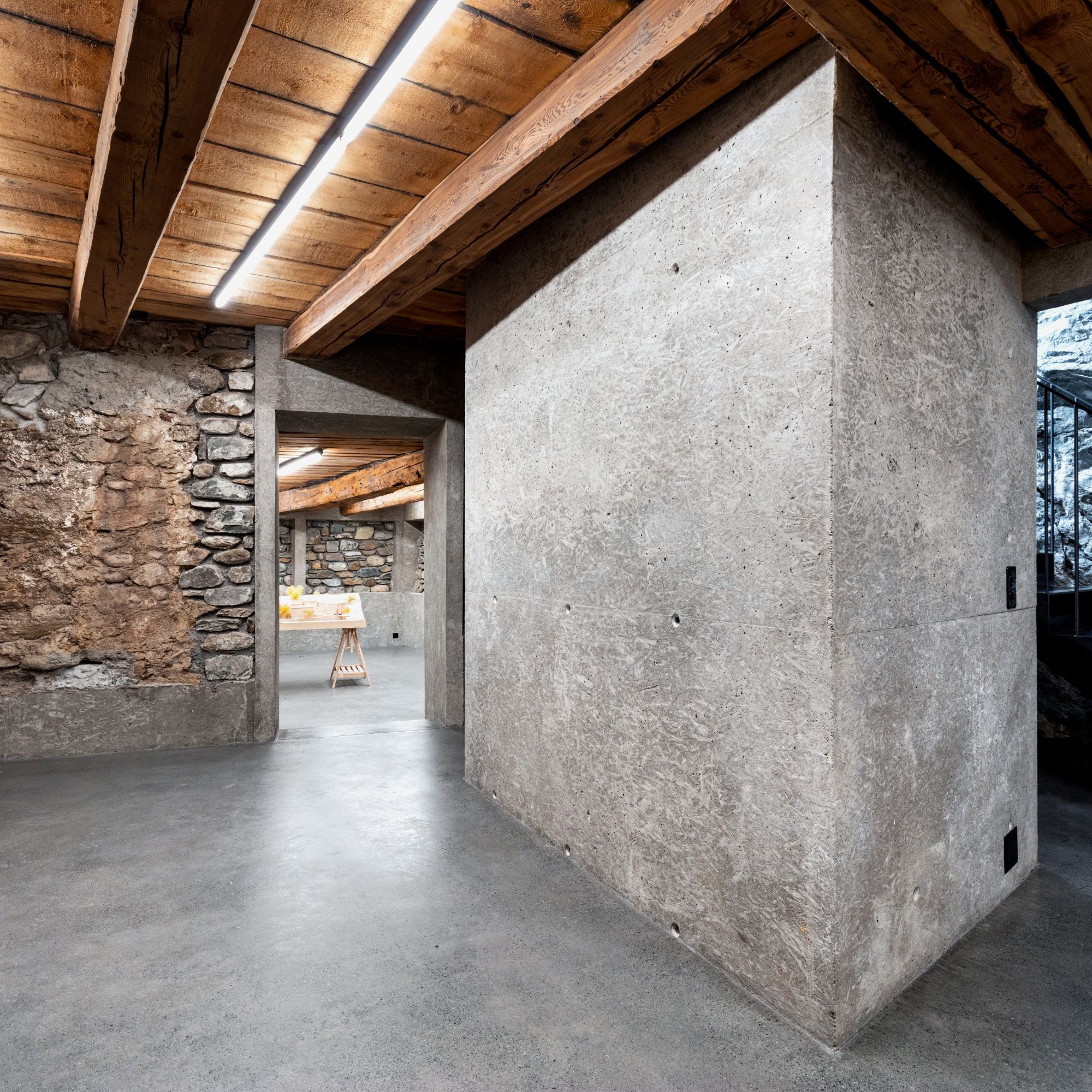 Chesa Della Santa, Untergeschoss: Unterfangung der traditionellen Mauerwerkswände, Sanitärkern aus Waschbeton, Untersicht des ursprünglichen Bodens in Lärche und Stahltreppe entlang der bestehenden Felswand.
