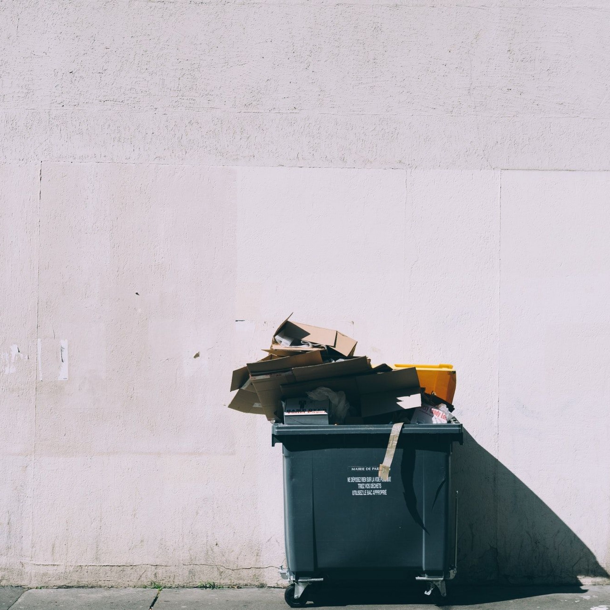 Übervolle Mülltonne vor weisser Wand