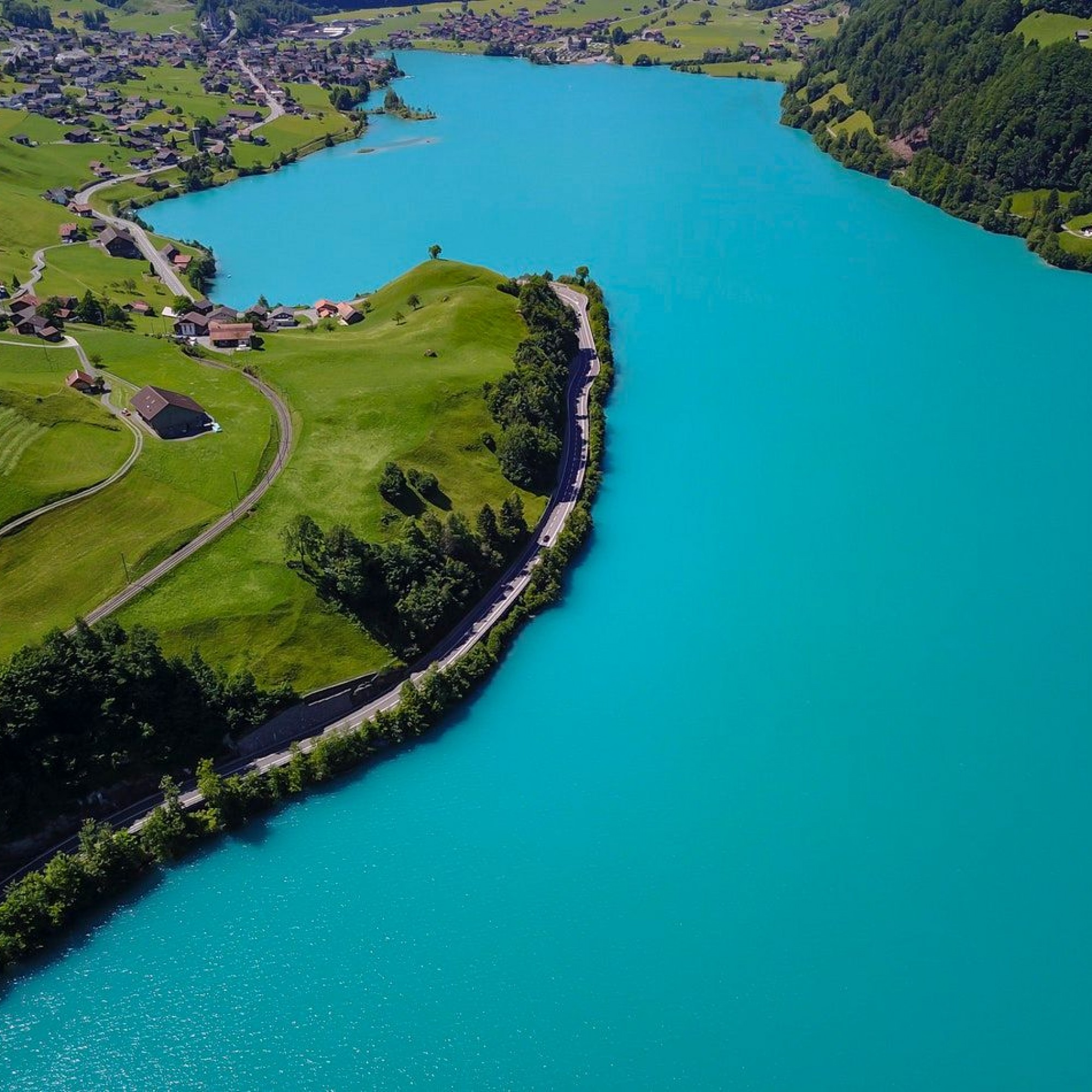 Atemberaubend blauer See mit grünen Matten und kleinem Dorf