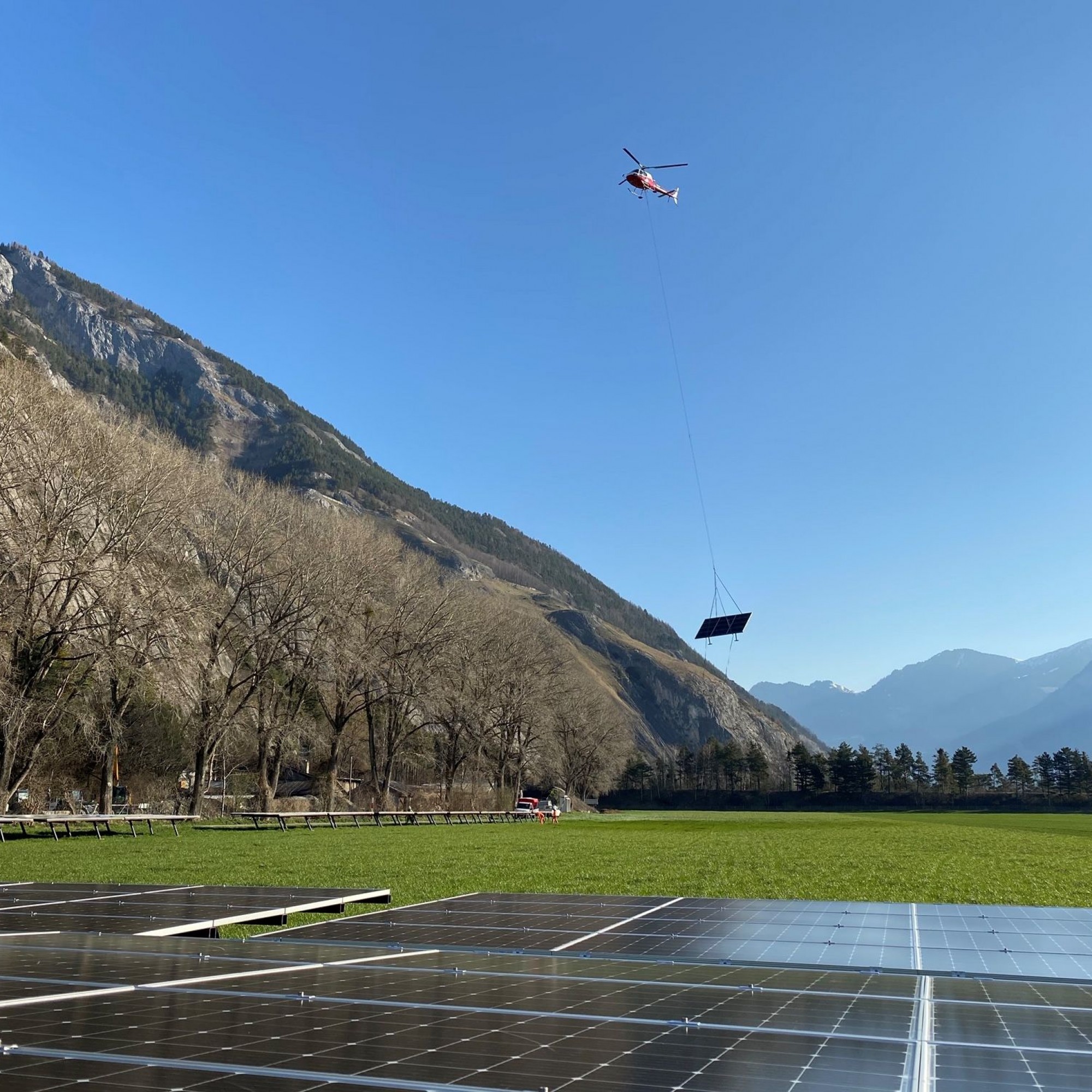 Helikopter fliegt Solarmodul vom Talboden in die Höhe.