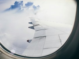Blick aus dem Flugzeugfenster auf Flügel und Wolken.