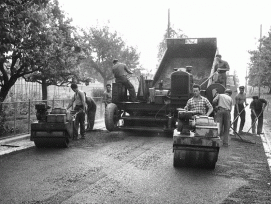 Bauarbeiter der Firma Cellere AG, St. Gallen teeren eine Strasse mit Hilfe einer Einbaumaschine, die Mischgut in einer Mulde aufnimmt und hinter der Maschine gleichmässig verteilt und verdichtet. Sommer 1956, o. O. (zvg) 1/11