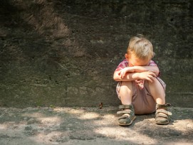 Trauriges Kind kauert auf dem Boden an einer Wand