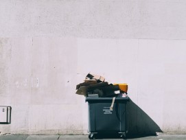 Übervolle Mülltonne vor weisser Wand